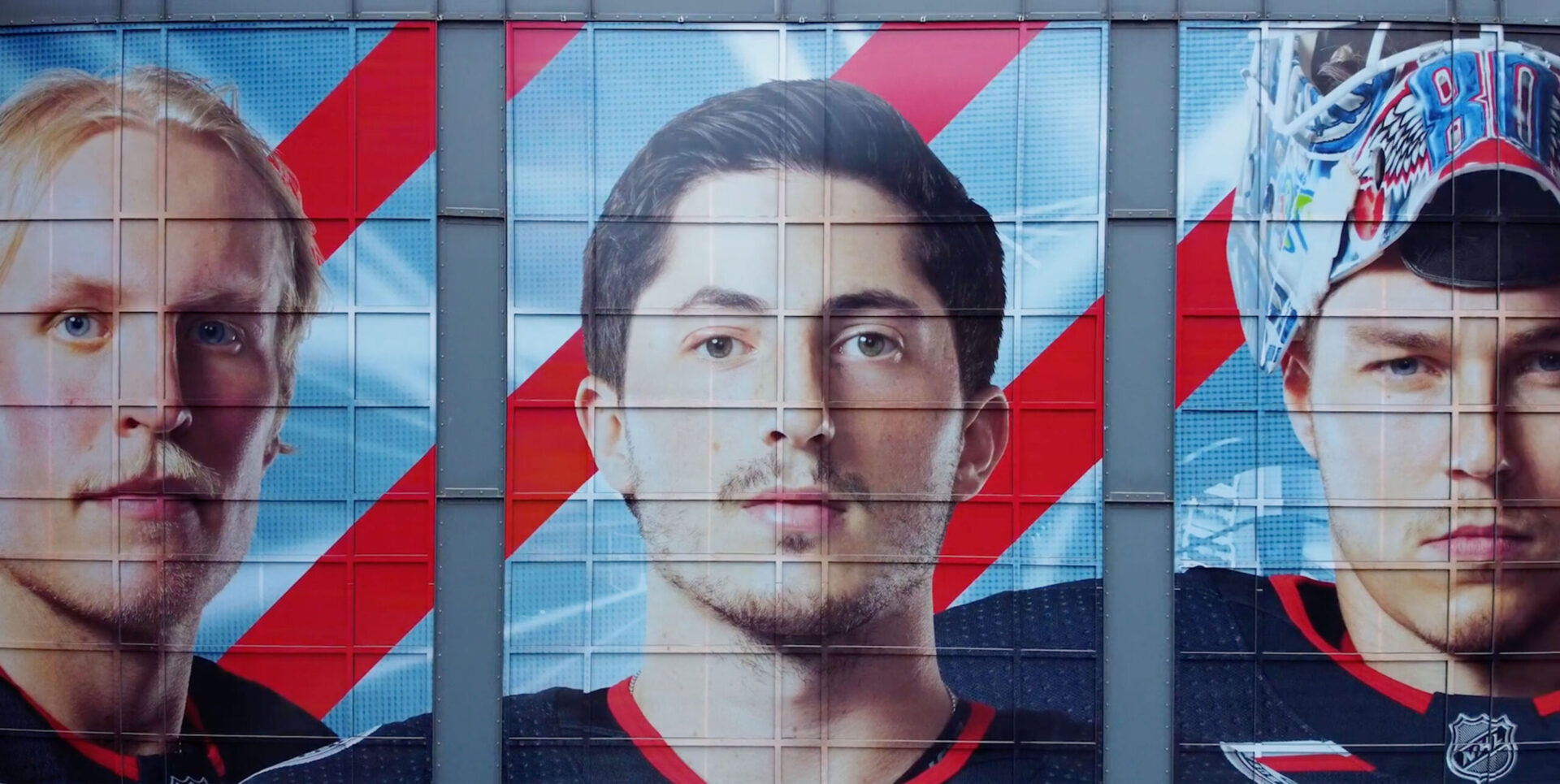 Large mural of Columbus Blue Jackets hockey players' faces, overlaid on dynamic red and blue stripes.