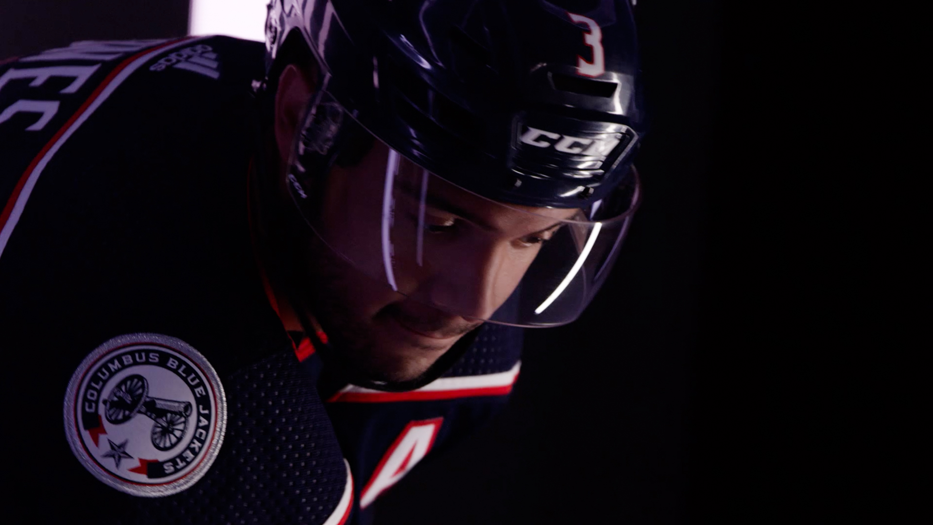 A darkened image of a hockey player in a Columbus Blue Jackets uniform, introspectively preparing for a game, with focused lighting emphasizing his concentration.