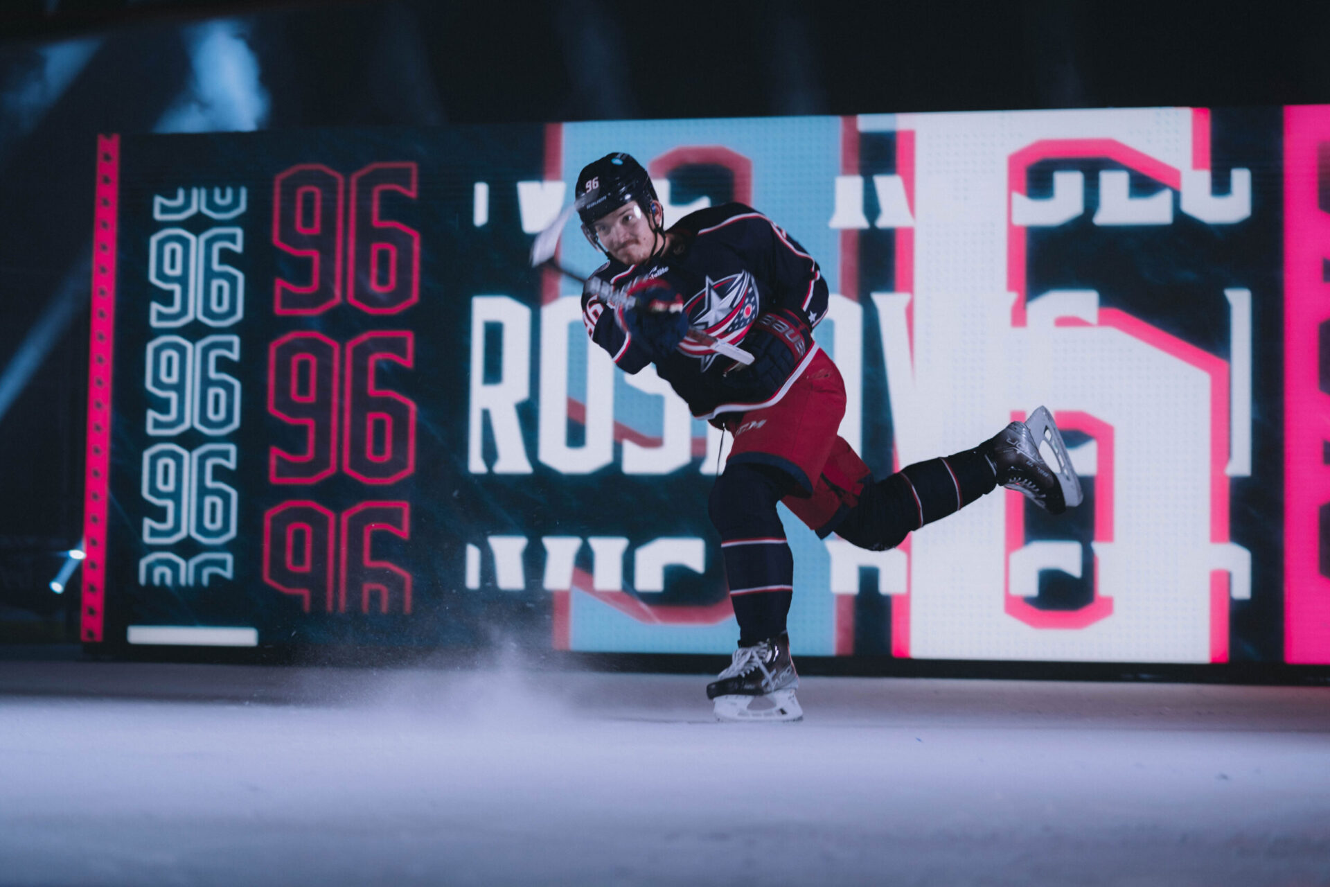 A hockey player in a red and blue uniform skating out with smoke around and a digital backdrop with the number '96'.