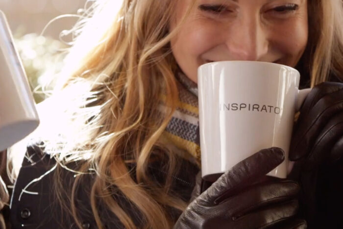 Smiling blonde woman sipping from a white Inspirato coffee mug