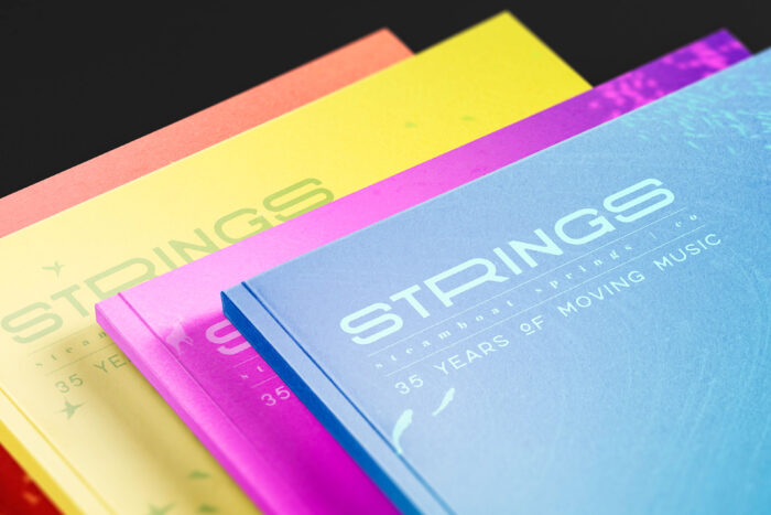 Colorful brochures stacked with the top blue one titled 'STRINGS 35 Years of Moving Music'.