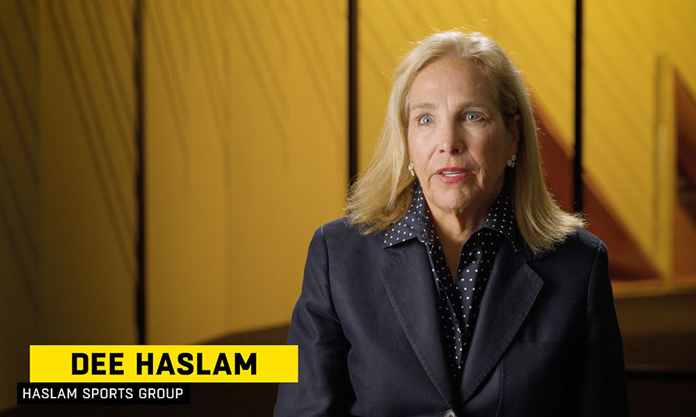 image of Dee Haslam, a woman with blue eyes and blonde hair wearing a suit being interviewed in front of a yellow backdrop
