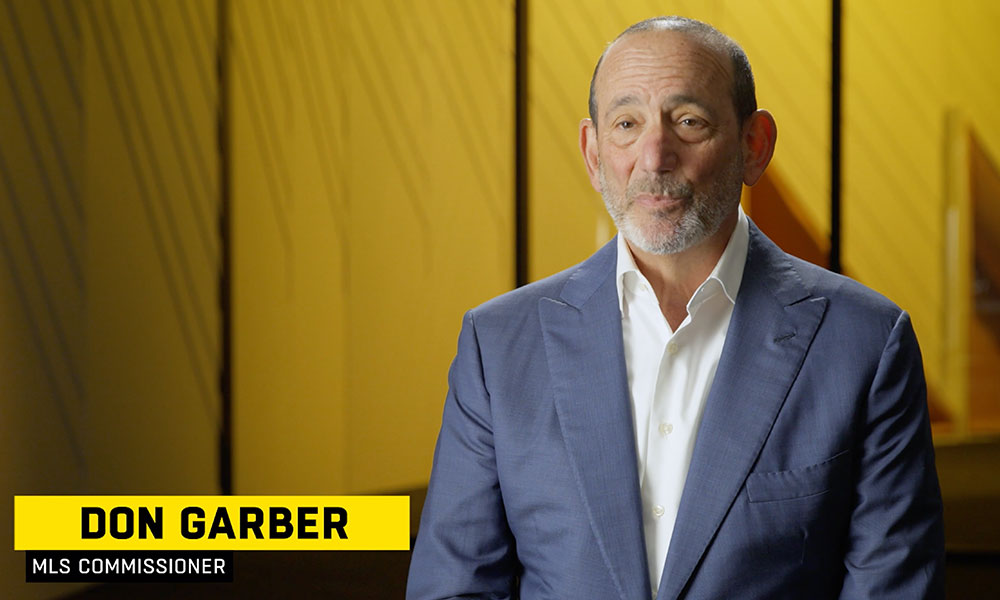 Image of a man in a blue suit jacket named Don Garber, MLS Commisioner against a yellow backdrop
