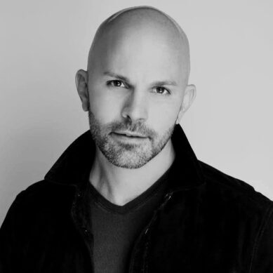 Black and white professional headshot of a bald man with a beard, dressed in black.